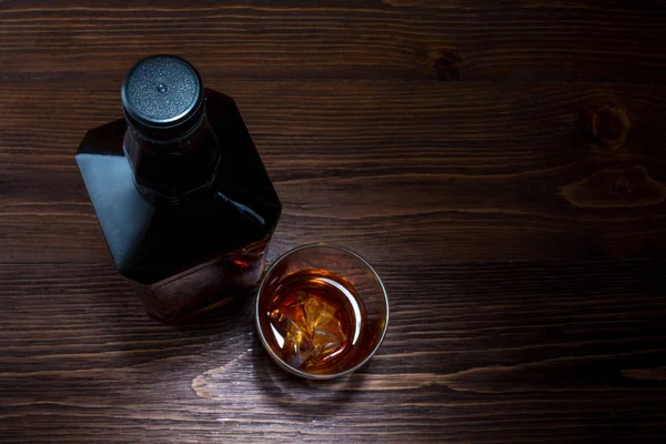 Whiskey bottle and whiskey glass with ice cubes on white wooden table