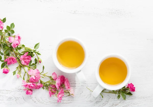 Dos tazas de té y una rama de rosas rosadas pequeñas . — Foto de Stock
