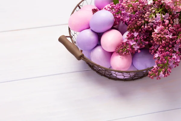 Uova di Pasqua e fiori lilla sul tavolo di legno rosa . — Foto Stock