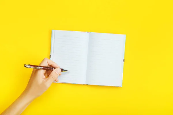 Mano con bolígrafo sobre cuaderno en blanco sobre fondo amarillo. Prepárate con espacio de copia para tus ideas . — Foto de Stock