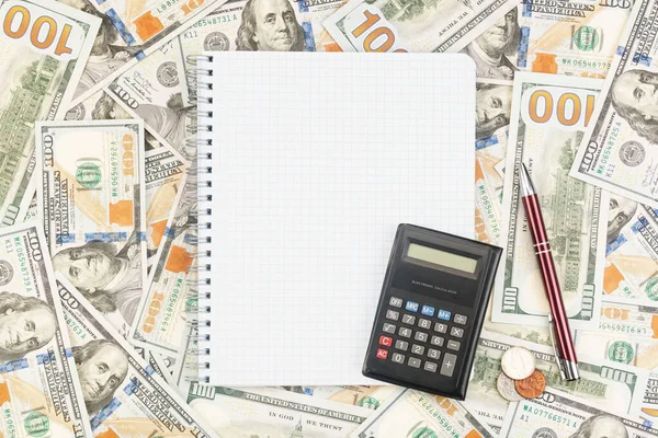 Note book with pen, coins and calculator on the background of dollar bills