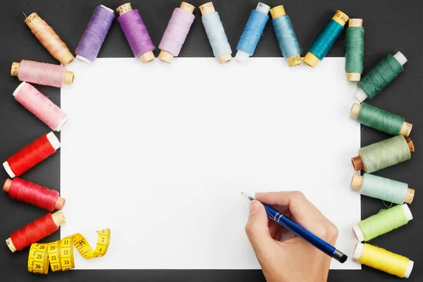 흰색 종이 위에 볼펜을 들고 색깔있는 실 코일 과 재단사 미터가 있는 손 — 스톡 사진