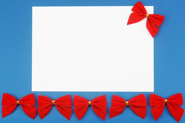 青い背景に赤い休日の弓と空白の白い紙. — ストック写真