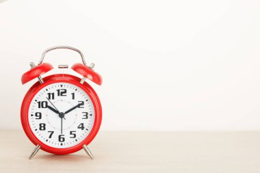 Kırmızı retro alarm saati, beyaz zemin üzerinde ahşap bir masa üzerinde geniş bir kadranla..