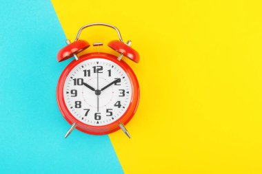 Red retro alarm clock with a big dial, on divided diagonally blue-yellow background clipart