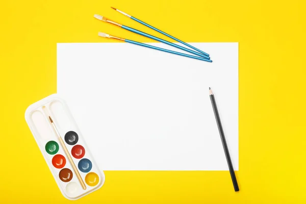Tomma papper med penna, penslar och färger på gul bakgrund — Stockfoto