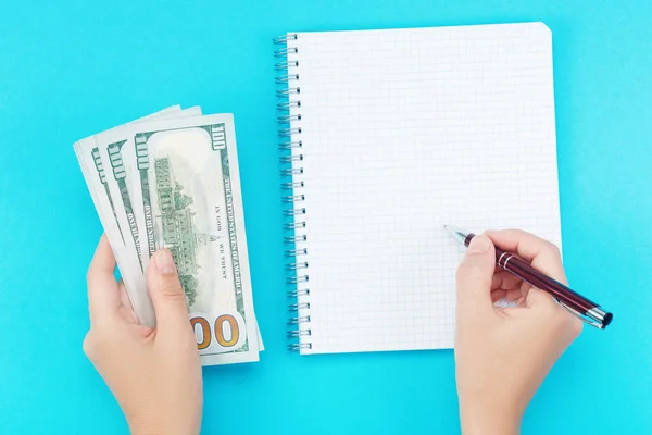 A woman holds money in her hand and writing in a notebook on a blue background — Stock Photo, Image