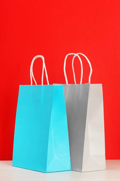 Modré a šedé nákupní nebo dárkové tašky na dřevěném stole na červeném pozadí — Stock fotografie