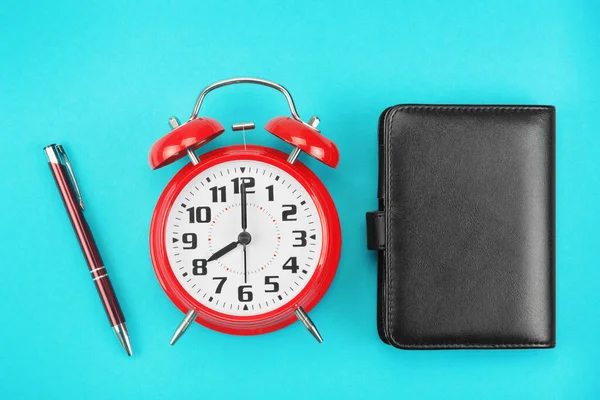 Red retro alarm clock with ballpoint pen and note booky blue background — Stock Photo, Image