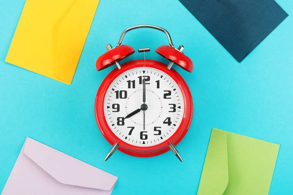 Colorful envelopes around the red alarm clock on a blue background — Stock Photo, Image