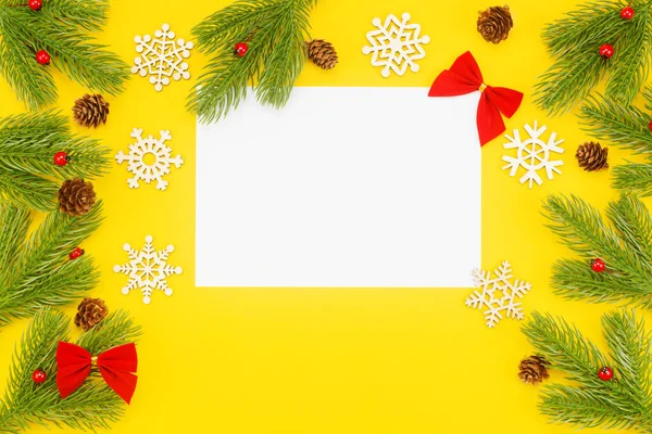 Borde navideño con ramas de abeto, ceniza de montaña, conos y un papel blanco en blanco sobre un fondo amarillo — Foto de Stock