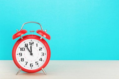 Kırmızı retro alarm saati, saat 12 'ye beş kala, mavi arka plandaki ahşap masada.