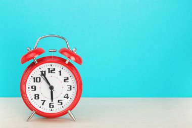 Altıya beş kala kırmızı retro alarm saati, mavi arka plandaki ahşap masada.