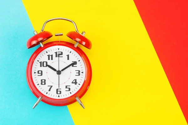 Reloj despertador retro rojo con una esfera grande, sobre fondo dividido diagonalmente azul-amarillo-rojo — Foto de Stock