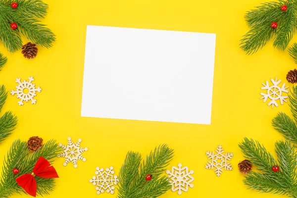 Borde navideño con ramas de abeto, ceniza de montaña, conos y un papel blanco en blanco sobre un fondo amarillo — Foto de Stock