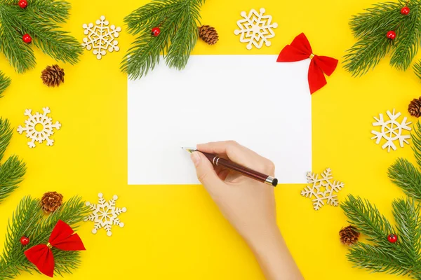 Mano con marcador sobre un papel blanco en blanco, borde de Navidad con ramas de abeto, ceniza de montaña, conos en un amarillo — Foto de Stock