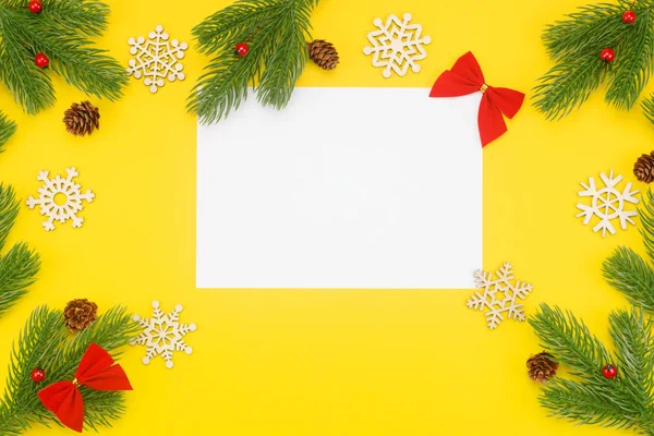 Borde navideño con ramas de abeto, ceniza de montaña, conos y un papel blanco en blanco sobre un fondo amarillo — Foto de Stock