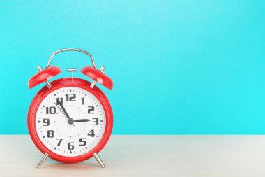 Kırmızı retro alarm saati, saat üçe beş kala mavi arka plandaki ahşap masada.