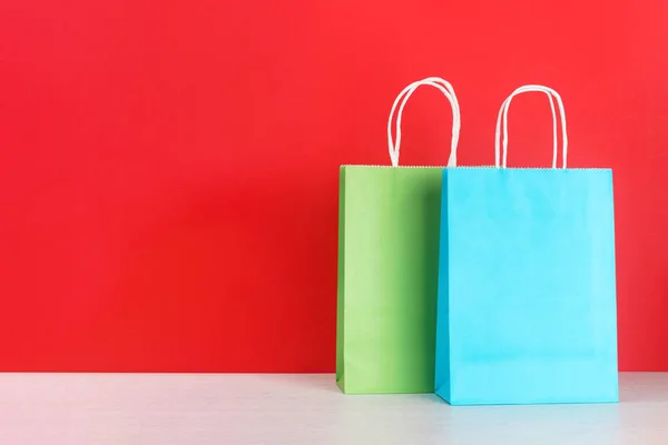 Bolsas de compras o de regalo azules y verdes sobre escritorio de madera sobre fondo rojo Imágenes de stock libres de derechos