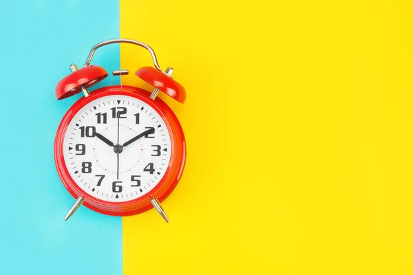 Red retro alarm clock with a big dial, on divided blue-yellow background Royalty Free Stock Images