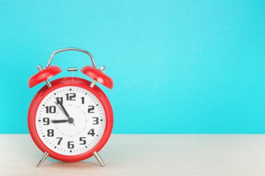 Kırmızı retro alarm saati, saat dokuza beş kala mavi arka plandaki ahşap masada.