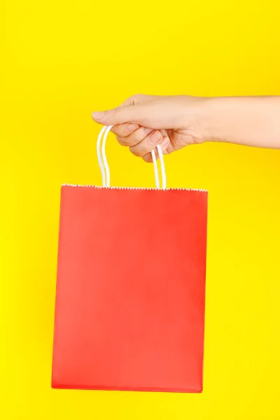 黄色の背景に赤いショッピングやギフトバッグを保持手 — ストック写真
