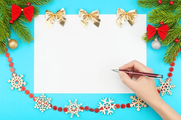 Mano con bolígrafo sobre un papel blanco en blanco con borde de Navidad que consta de ramas de abeto, juguetes de Navidad — Foto de Stock