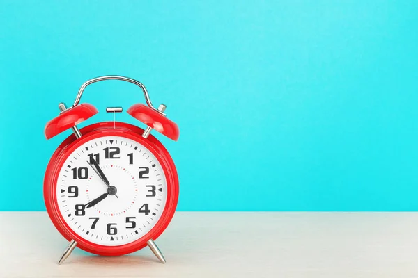 Red retro alarm clock with five minutes to eight oclock, on wooden table on a blue background — Stock Photo, Image