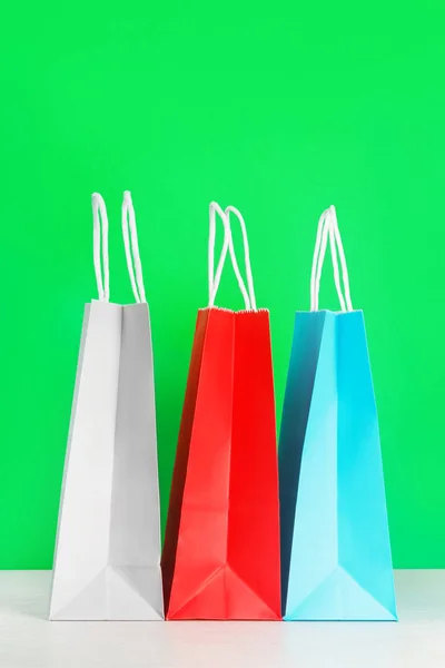 Colorful shopping or gift bags on wooden desk against green background.