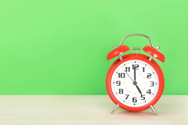 Red retro alarm clock with five oclock, on wooden table on a green background — Stock Photo, Image