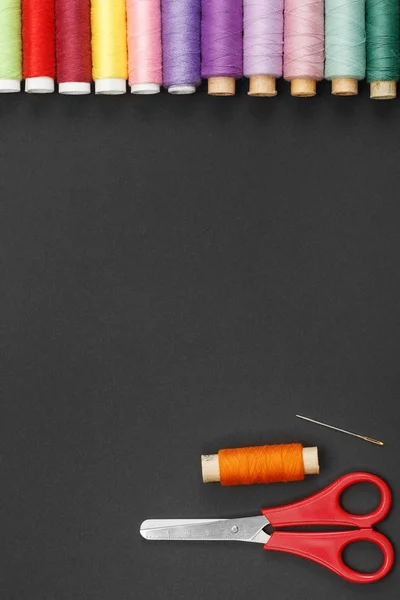 Farbige Fadenspulen, Schere und Nadel auf schwarzem Hintergrund. — Stockfoto