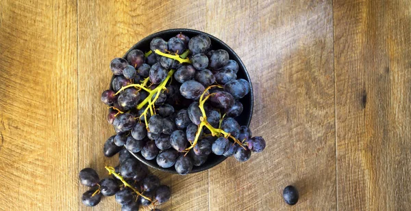 Raisins noirs dans un bol sur fond de bois chaud . — Photo