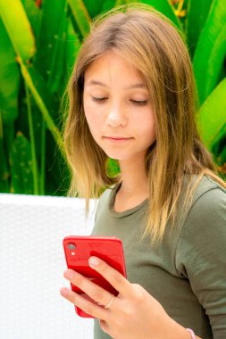 Genç bir kız akıllı telefonuyla dışarıda oturuyor.