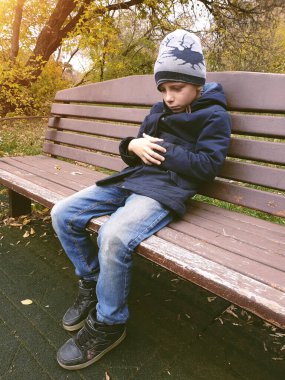 Üzgün çocuk bankta tek başına oturuyor.