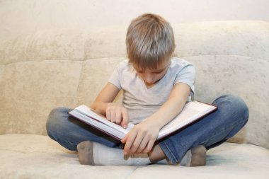 Küçük çocuk bej kanepede oturup kitap okurken uyuyakaldı. Zor eğitim süreci kavramı