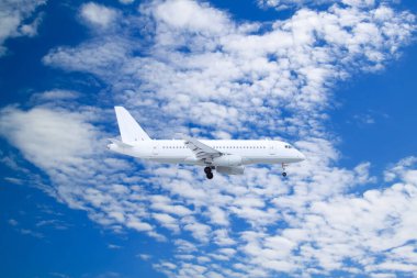 Beyaz yolcu uçağı, beyaz bulutların ve mavi gökyüzünün doğal arka planıyla karaya çıkar.