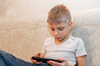 Küçük çocuk evde oturuyor ve telefonuyla oyun oynuyor.