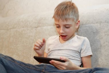 Mutlu küçük çocuk evde oturup telefonuyla oyun oynuyor.