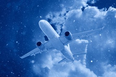 Beyaz yolcu uçağı kar altında gökyüzündeki güzel uğursuz bulutların arka planına doğru uçar. Kış aylarında moda olan 2020 'nin klasik mavi rengine bürünür.