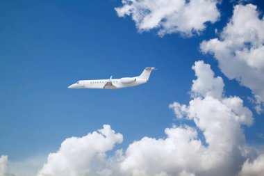 Beyaz özel jet iş jeti mavi gökyüzündeki güzel beyaz bulutların üzerinde uçuyor.