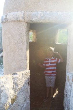 Mutlu çocuk kendini orta yaşlı savaşçı olarak selamlıyor. Antik şehrin kalesinin duvarında bekçi deliğinde.