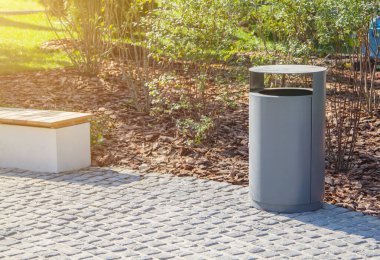 arkasında malçlı manzara ile gri minimalist çöp kutusu ve ahşap Park tezgah