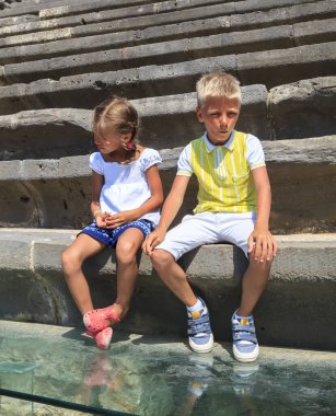 Türkiye 'nin Side kentindeki antik amfitiyatronun merdivenlerinde oturan yorgun çocuk ve kız çocuğu