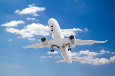 Beyaz yolcu uçağı iniş takımlarını indirdi ve beyaz bulutların ve mavi gökyüzünün arka planıyla karaya çıkıyor.