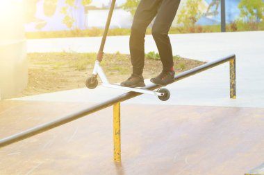 Dublör tekmeli scooter kaykay parkında metal rampanın kenarında kayıyor.