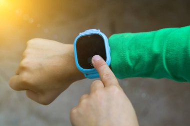 Çocuk işaret parmağıyla ekrana basan dijital saate bakıyor. Modern çocuk teknolojileri. Çocuklar için GPS izleyici, çocuk takibi ve ebeveyn denetimi kavramı.