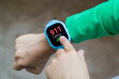 Küçük çocuk işaret parmağıyla ekranı tıklatarak dijital akıllı saat için acil durum çağrısı yapıyor. Modern çocuk teknolojileri. Çocuklar için GPS izleyici, çocuk takibi ve ebeveyn denetimi kavramı.