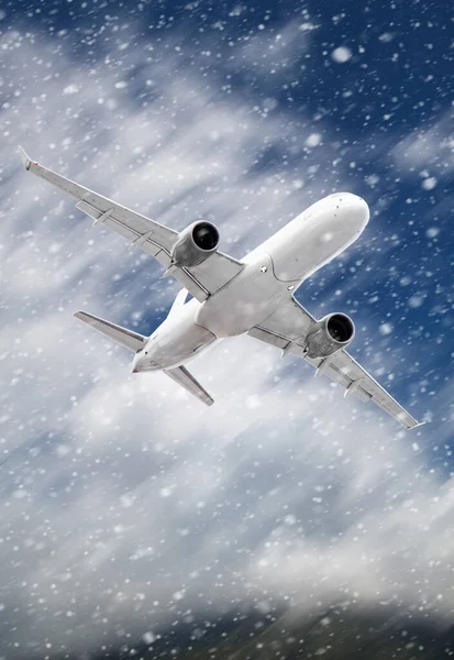 white passenger plane hurtles through rushing snow against a backdrop of mountains with white clouds.  Landscape with airplane, mountains and sky with white clouds in winter.