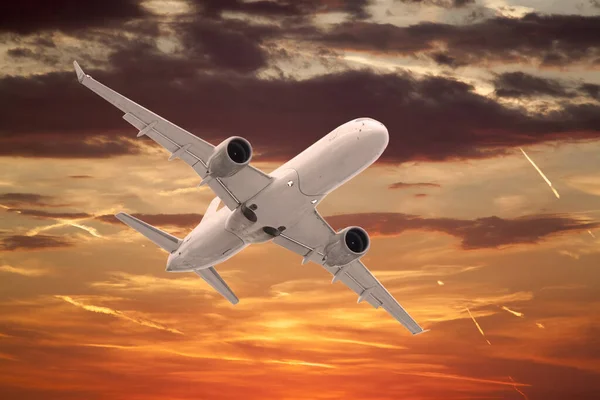 白色的客机在美丽的日落天空的背景下飞行 天空是橙色的 有云彩和凝结的痕迹 — 图库照片