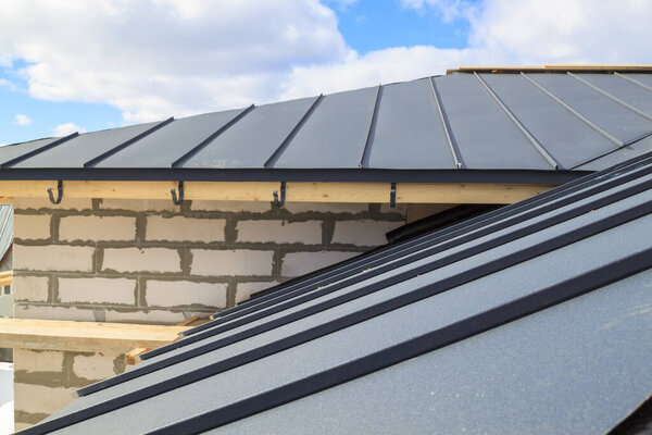 крупный план строительных лесов и строящегося дома с серой складной крышей на гидроизоляционном слое
